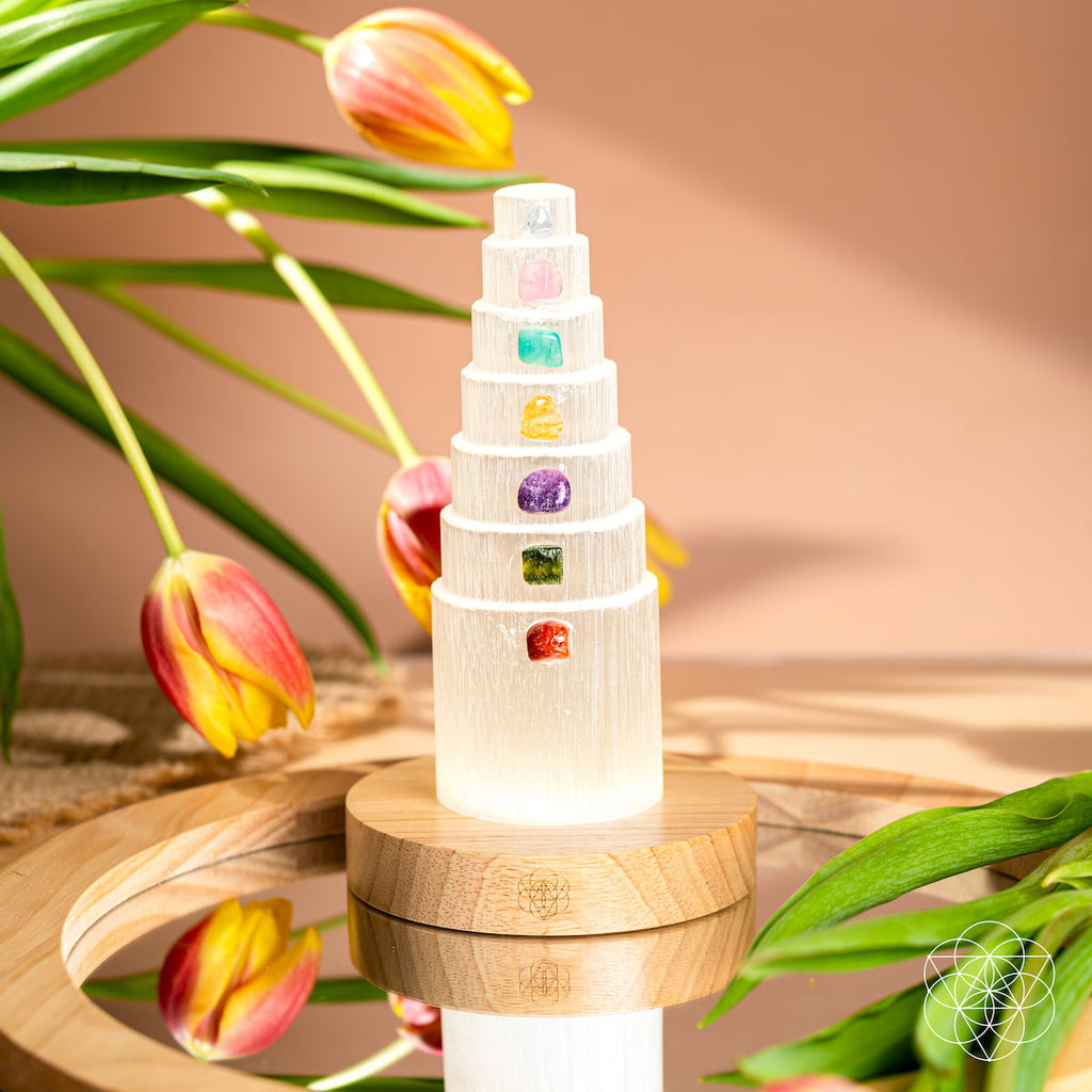 Selenite lamp with seven colored crystal accents on a mirrored tray beside yellow and pink tulips.
