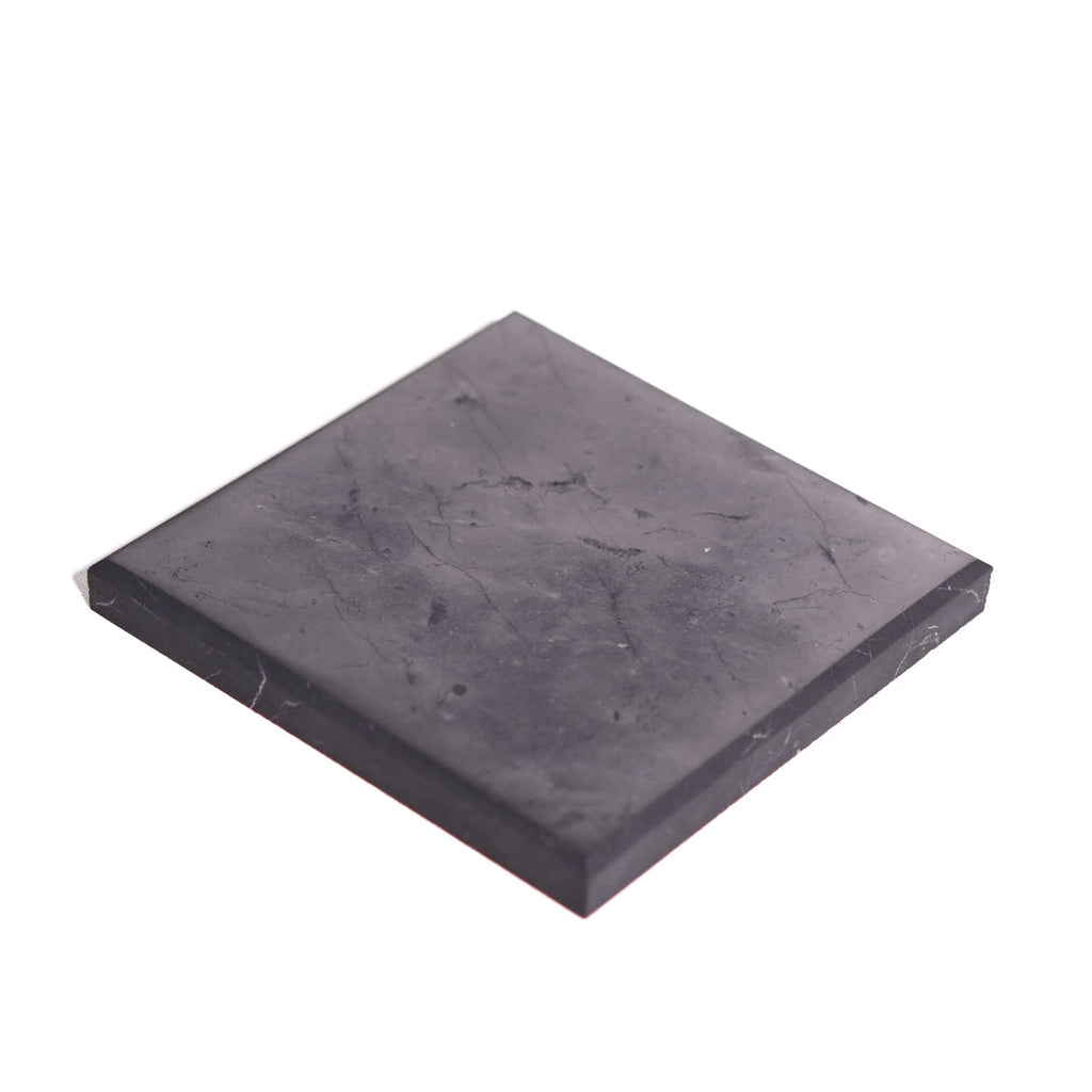 Square shungite plate positioned diagonally on white, showing its flat surface and straight dark edges.

