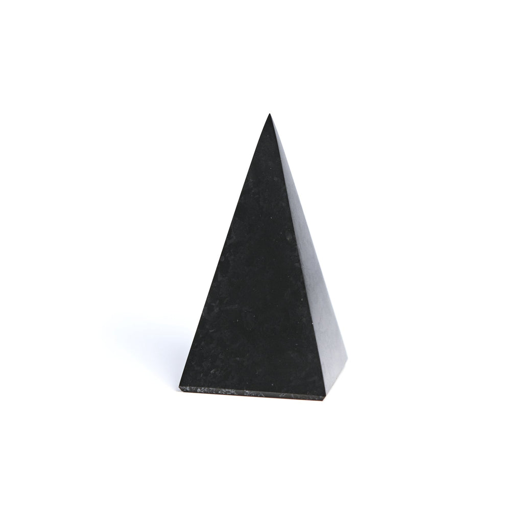 Tall black shungite pyramid standing upright on white, showing its pointed top and triangular faces.
