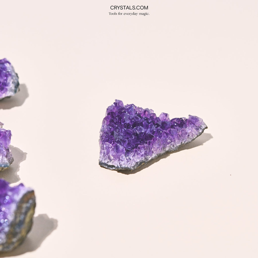 Triangular purple amethyst cluster on pale pink with other clusters partly visible along the left edge.
