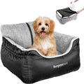 A small tan and white dog sits in a black and gray BurgeonNest pet bed with a gray sherpa lining. A small inset in the top right shows a person's hands stretching the bed to demonstrate its flexibility.