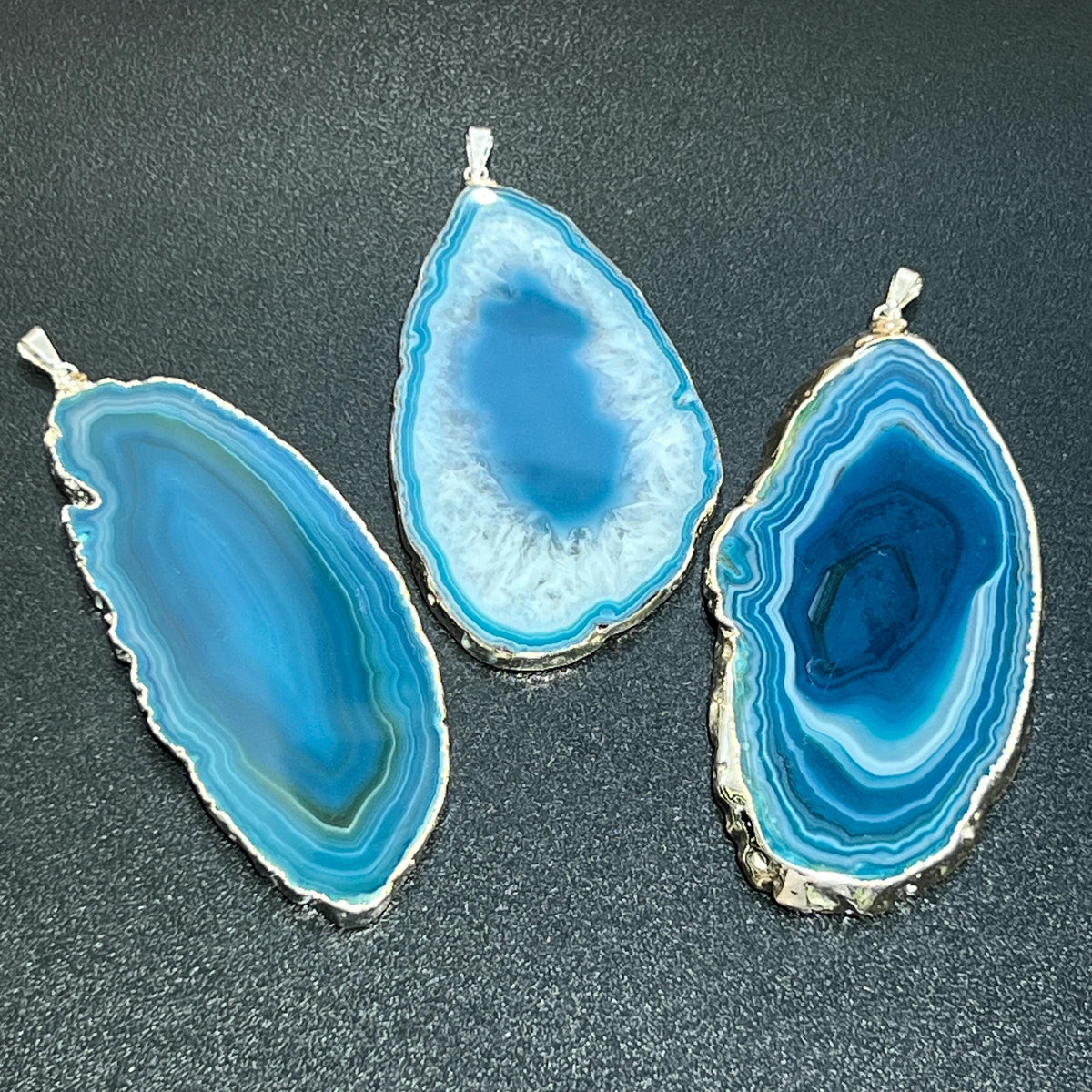 Three large teal agate slice pendants with silver-plated edges, banded patterns, and contrasting centers.
