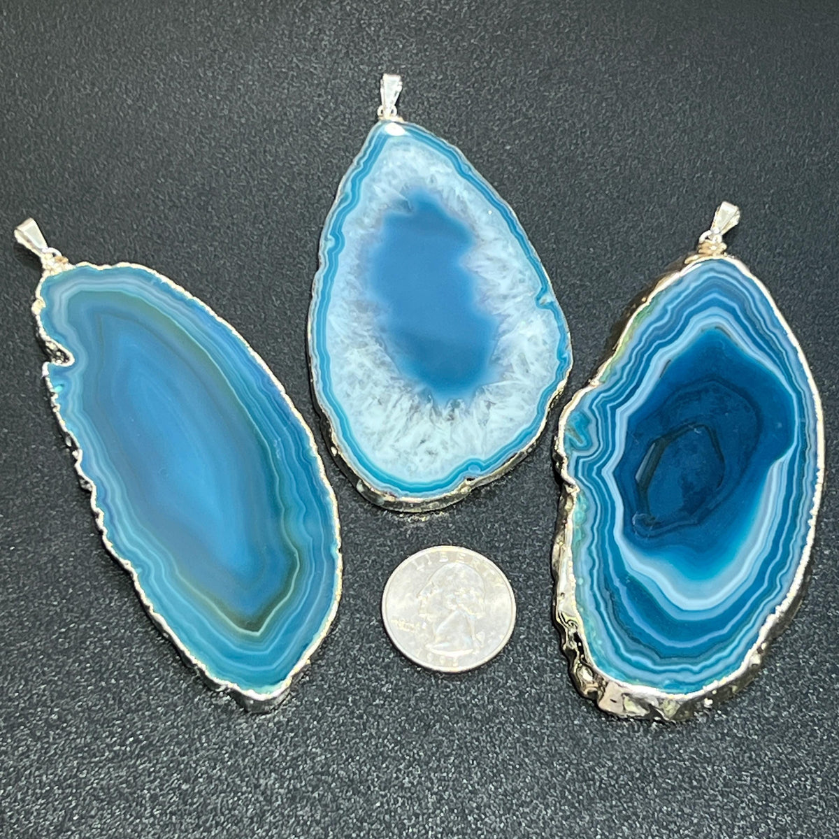 Three blue agate pendants on a dark surface with a coin for scale.
