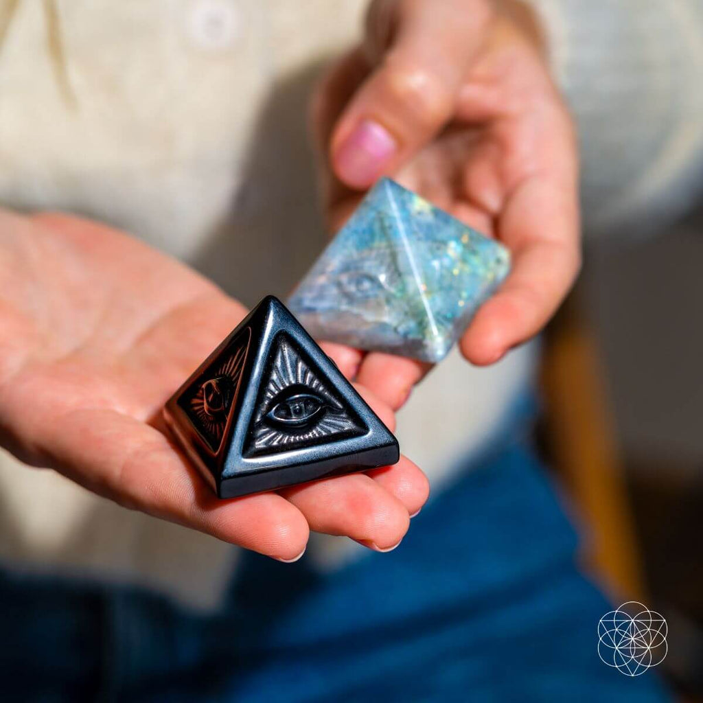 Person holding a black obsidian eye pyramid in one hand and a labradorite eye pyramid in the other.
