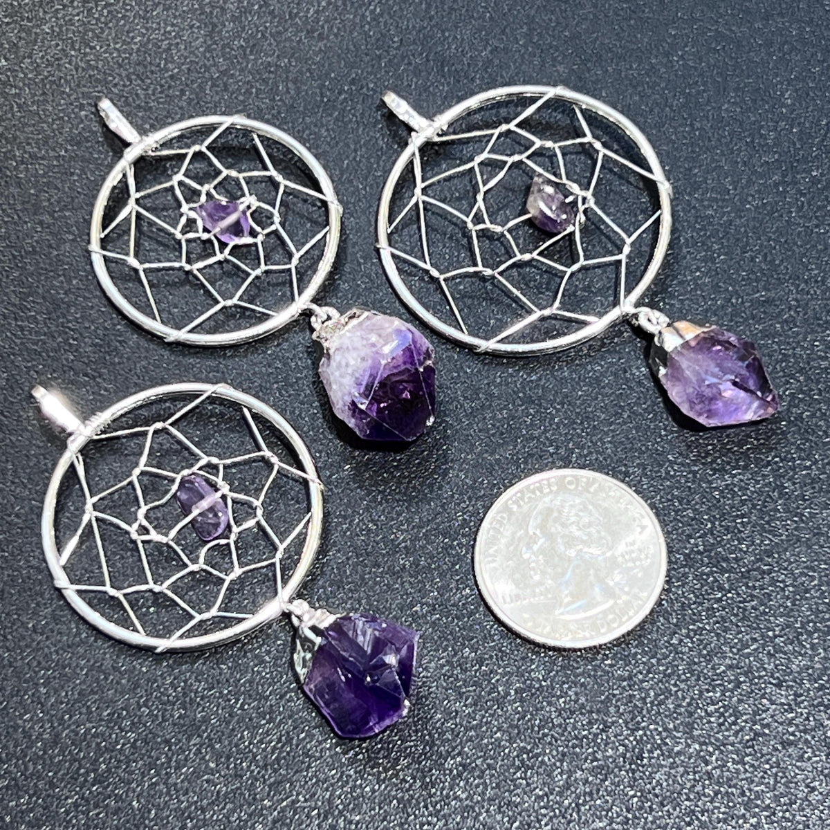 Three amethyst dreamcatcher pendants with circular silver-plated web designs beside a quarter for scale