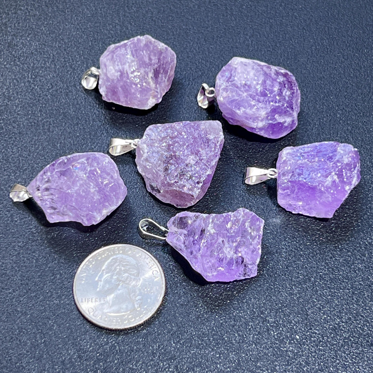 Six raw lavender amethyst pendants with silver-tone bails beside a quarter for size comparison.
