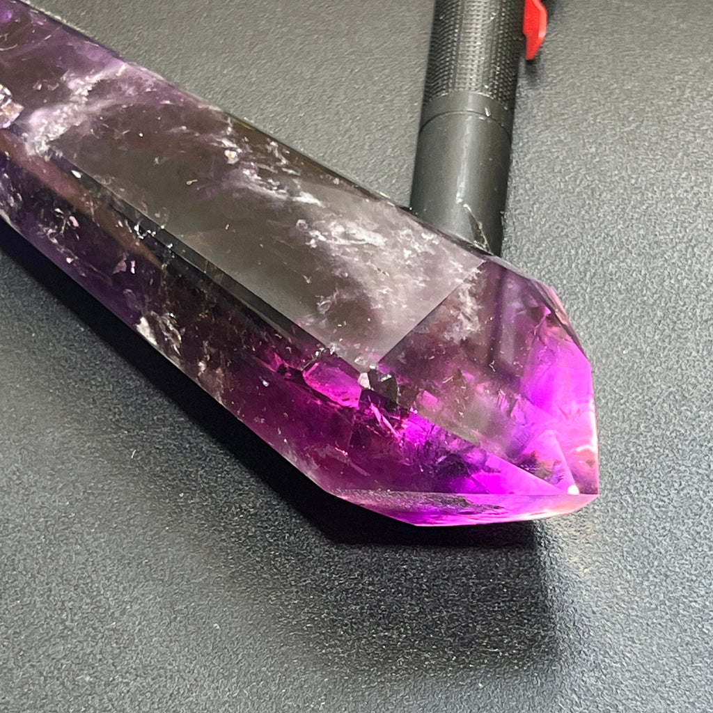 Close-up of an amethyst tower lying beside a flashlight, with its faceted tip glowing bright purple