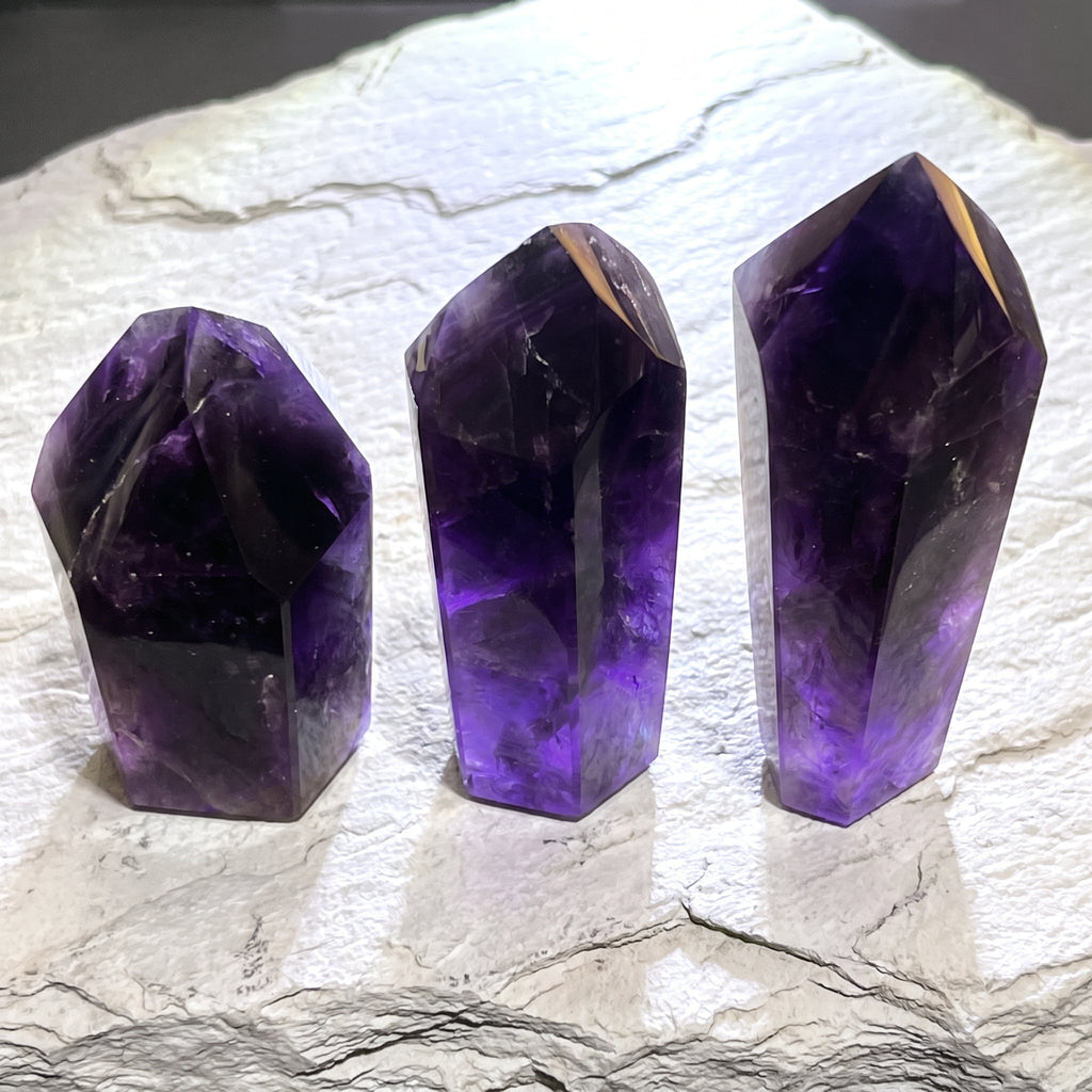 Three polished dark amethyst towers with pointed tops standing on a white stone slab