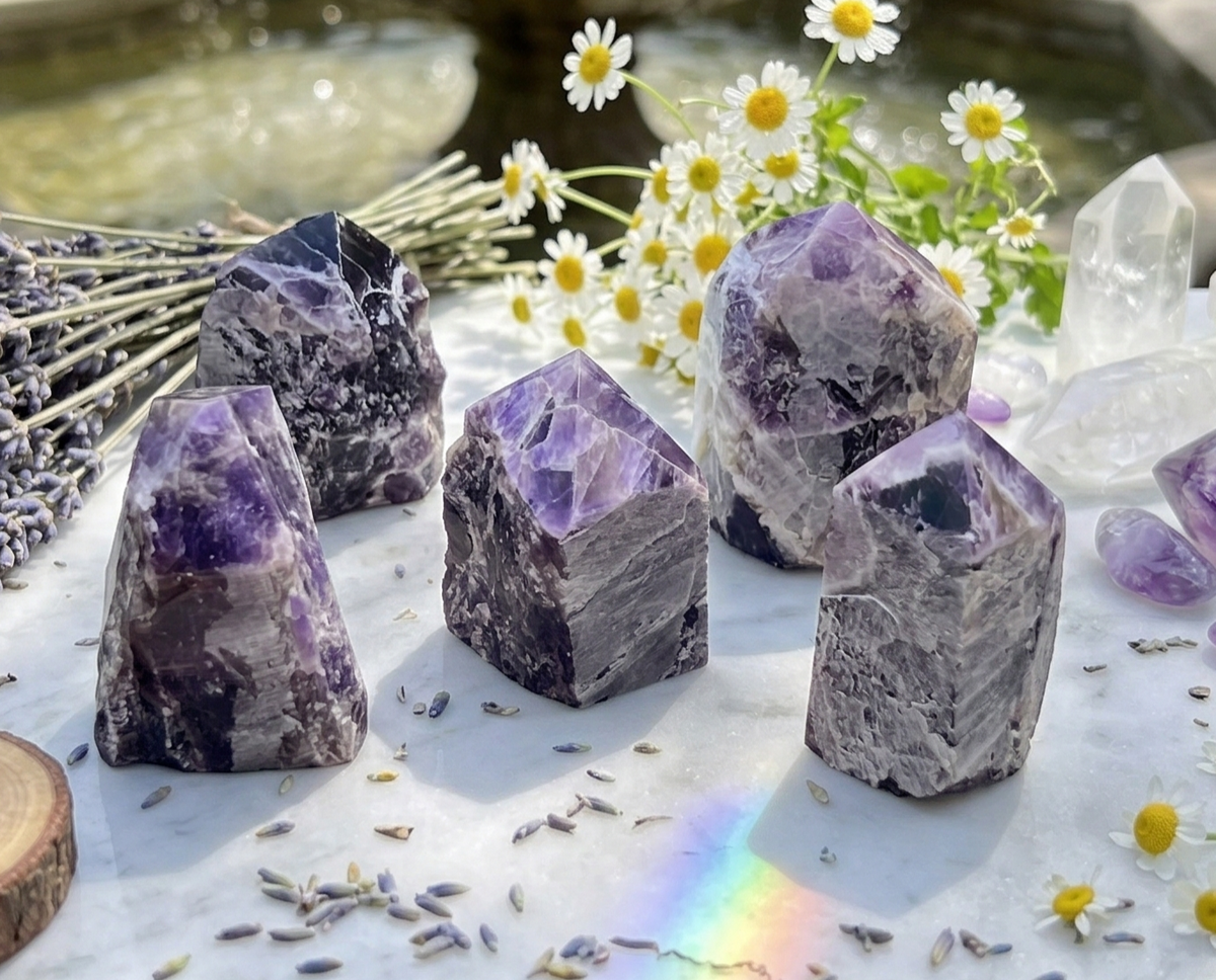 Five banded amethyst towers displayed with white flowers, lavender sprigs, and clear crystals on a pale tabletop.
