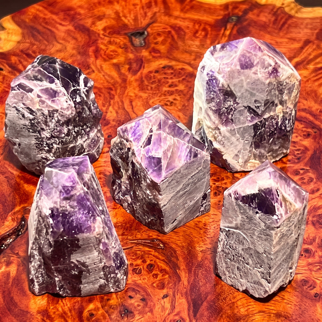 Five banded amethyst towers with polished purple points displayed on reddish patterned wood.
