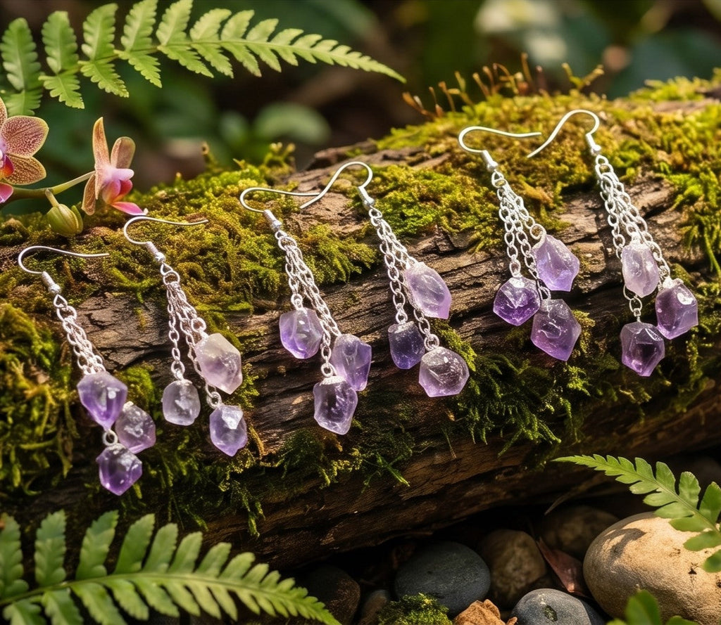 Three pairs of amethyst triple crystal earrings with silver-colored chains displayed on a mossy log among ferns.