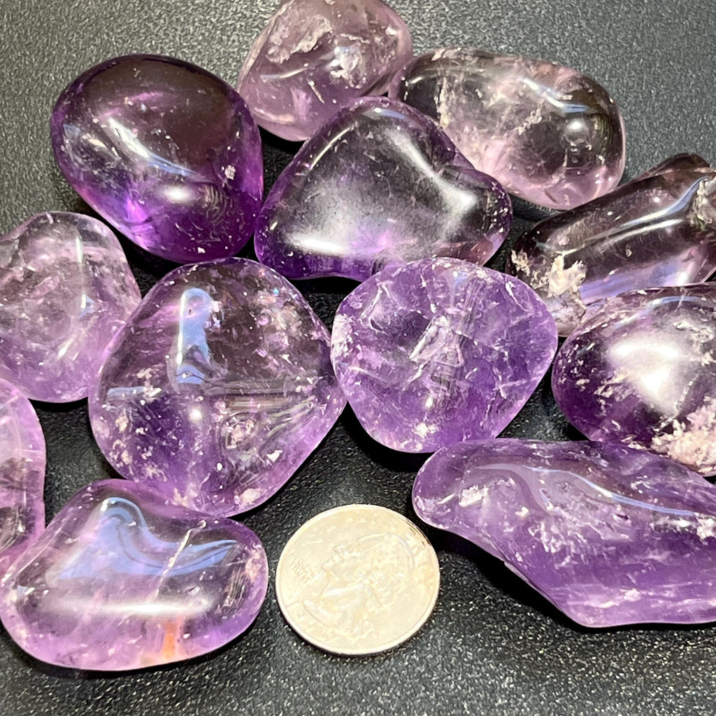 Large purple amethyst tumbled stones with glossy surfaces beside a coin for size comparison.