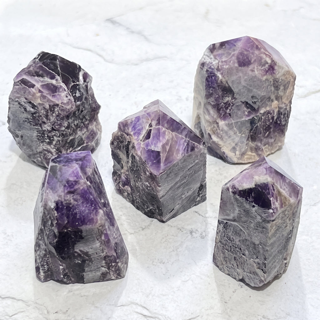 Five purple and pale banded amethyst point towers arranged on a white veined surface.
