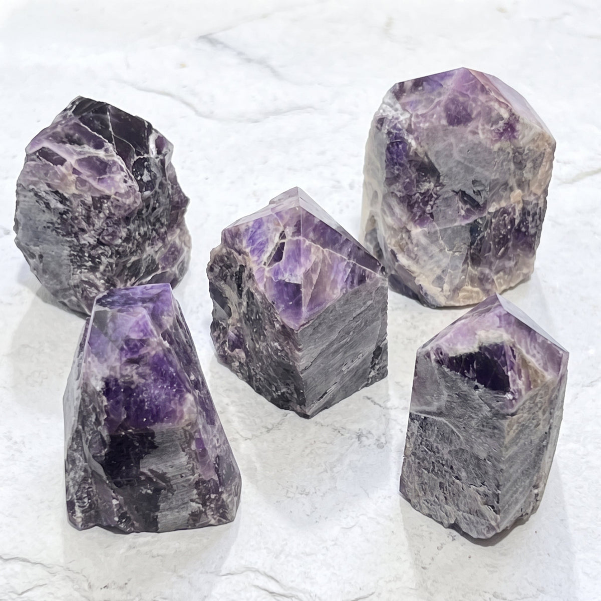 Five purple and pale banded amethyst point towers arranged on a white veined surface.
