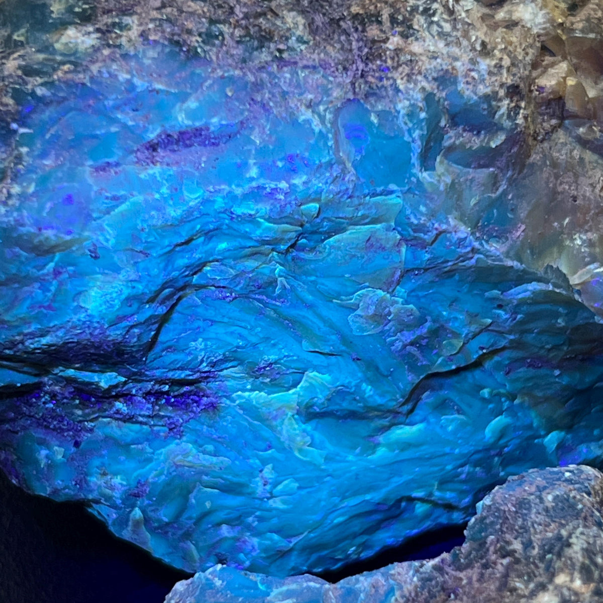 Detailed view of cracks and layered textures in black amber glowing bright blue with violet patches under UV light