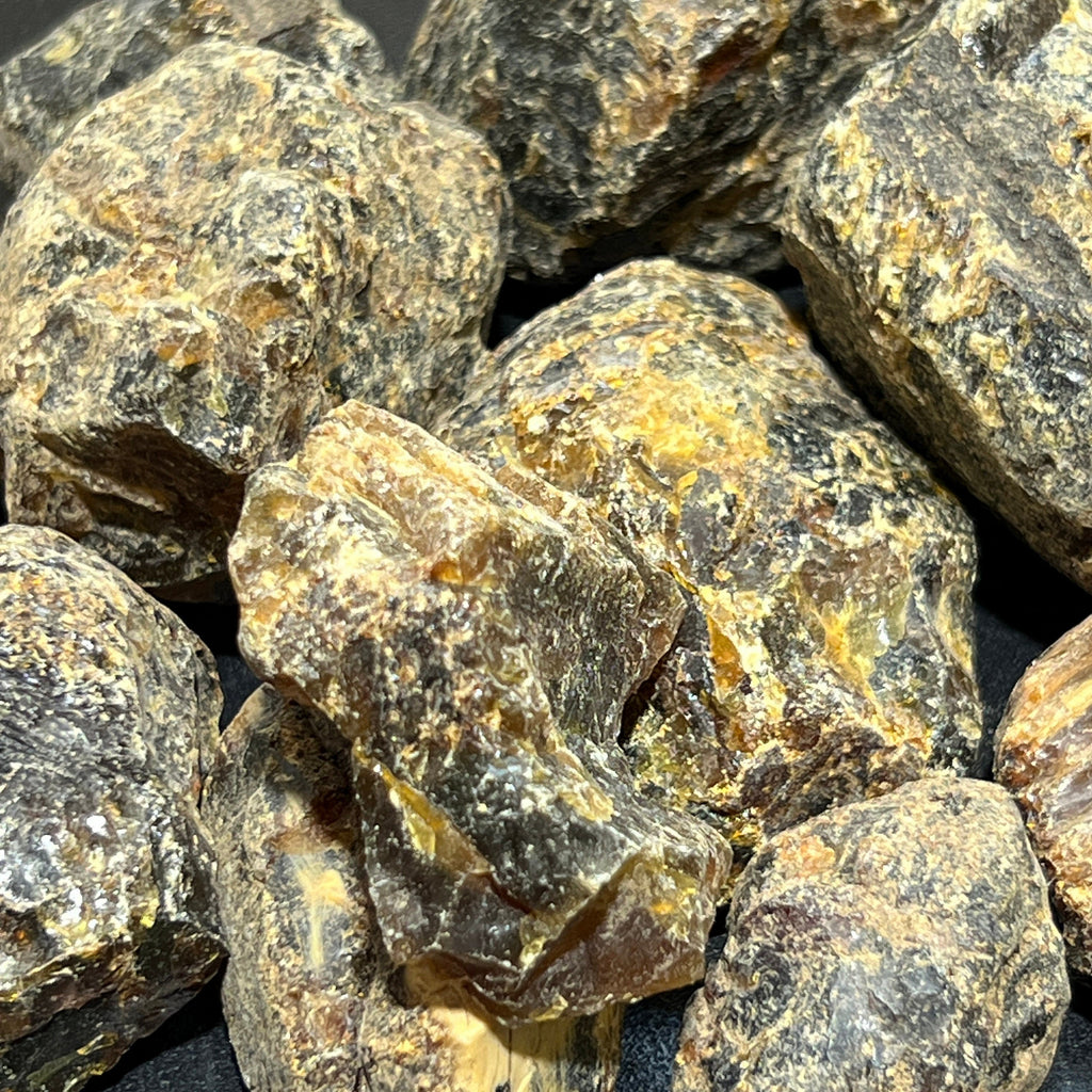 Close-up of uneven black amber surfaces with dark brown fractures and yellow-gold patches