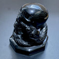Glossy black obsidian skull carving with a coiled snake, detailed scales and a shaped base