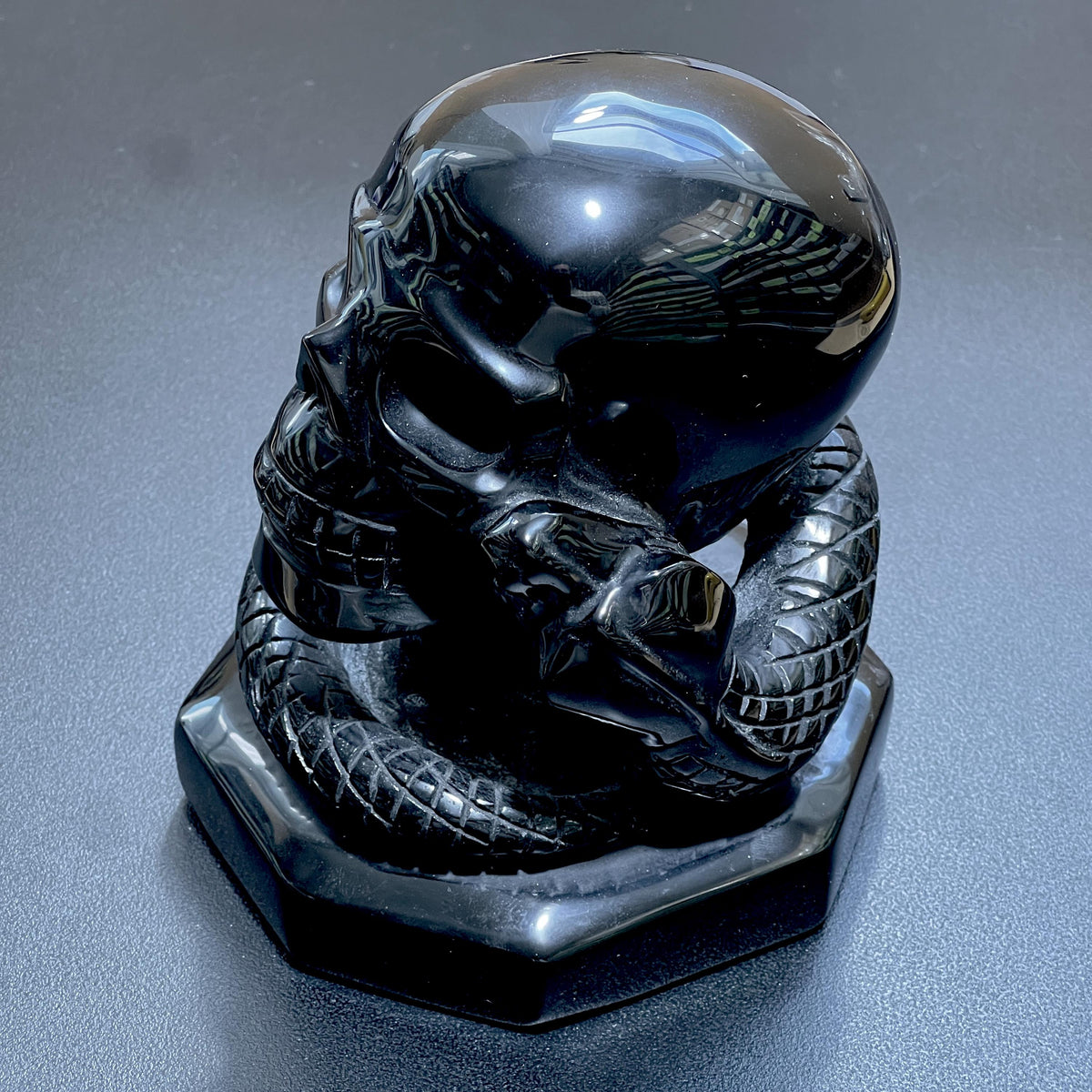 Glossy black obsidian skull carving with a coiled snake, detailed scales and a shaped base