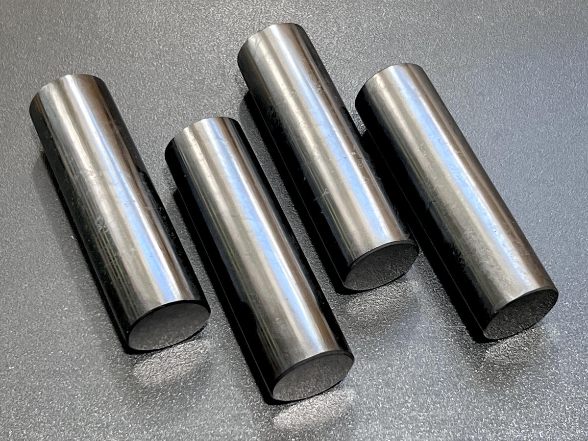 Four polished black shungite cylinder rods with reflective sides and flat circular ends on a dark surface.
