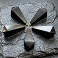 Five faceted black shungite pendulum point pendants with gold-colored hanging loops arranged on textured slate.
