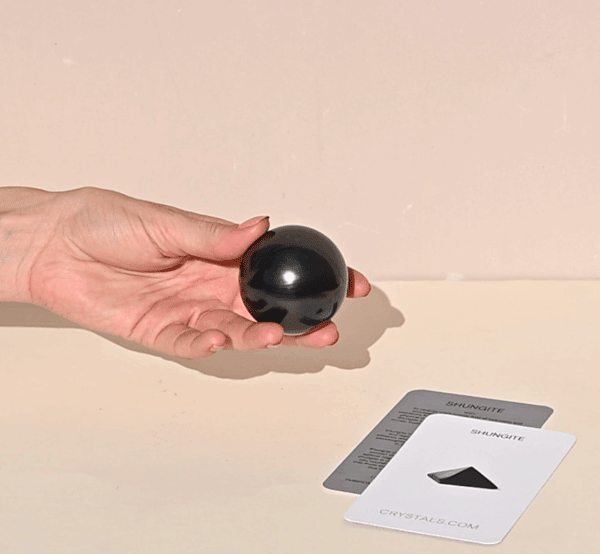 Small polished black shungite sphere resting in an open hand beside Shungite Collector's Cards.
