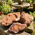 Three rough carnelian agate boulders with brown outer surfaces and exposed orange interiors beside a garden fountain