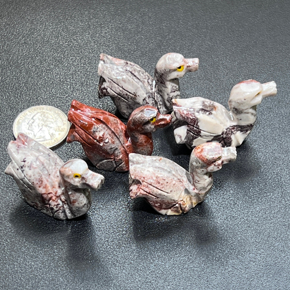 Five carved soapstone ducks with yellow eyes and marbled cream, gray and rust colors beside a coin