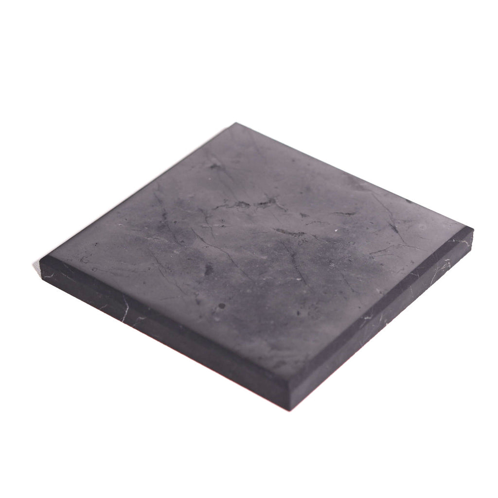 Angled view of a charcoal-black square shungite plate showing individual surface markings on a white background.
