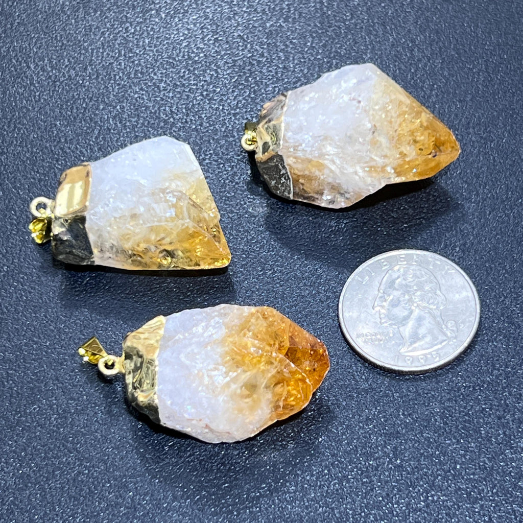 Three white and golden citrine crystal point pendants with gold-plated fittings beside a quarter for size comparison.