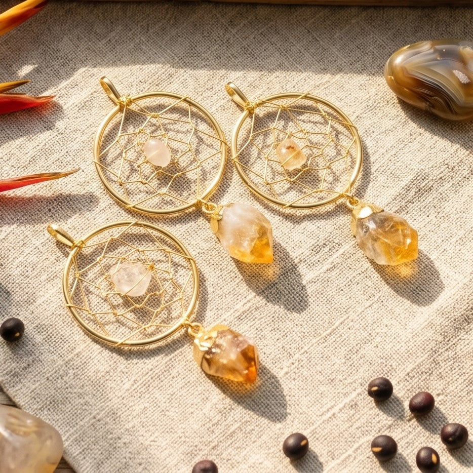 Three gold-plated citrine dreamcatcher pendants arranged on cream fabric in sunlight.
