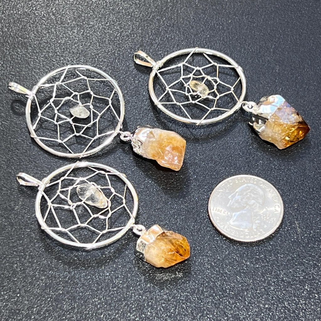 Three silver-plated citrine dreamcatcher pendants beside a quarter for size comparison on a dark textured background.
