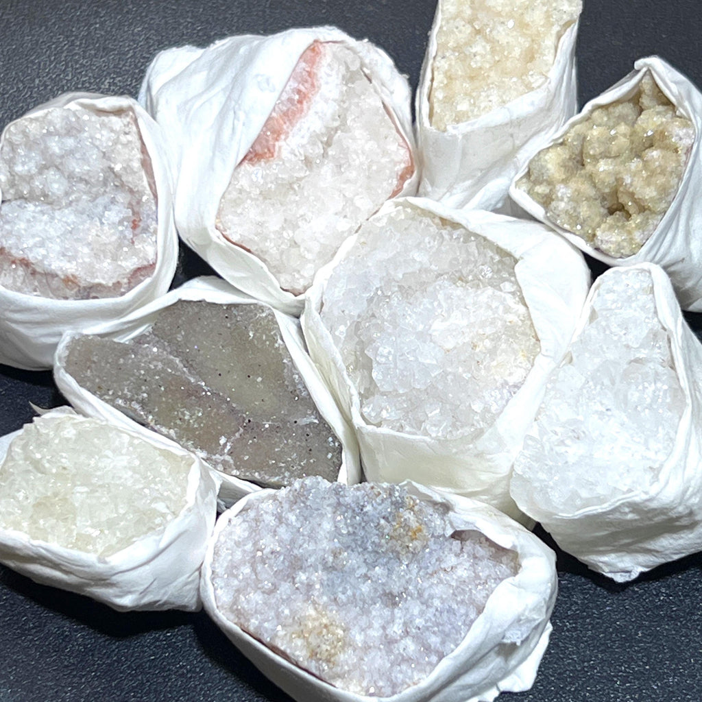 Assorted rough druzy crystal clusters in white, cream, gray and pale purple, individually wrapped in white paper