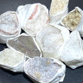 Assorted rough druzy crystal clusters in white, cream, gray and pale purple, individually wrapped in white paper