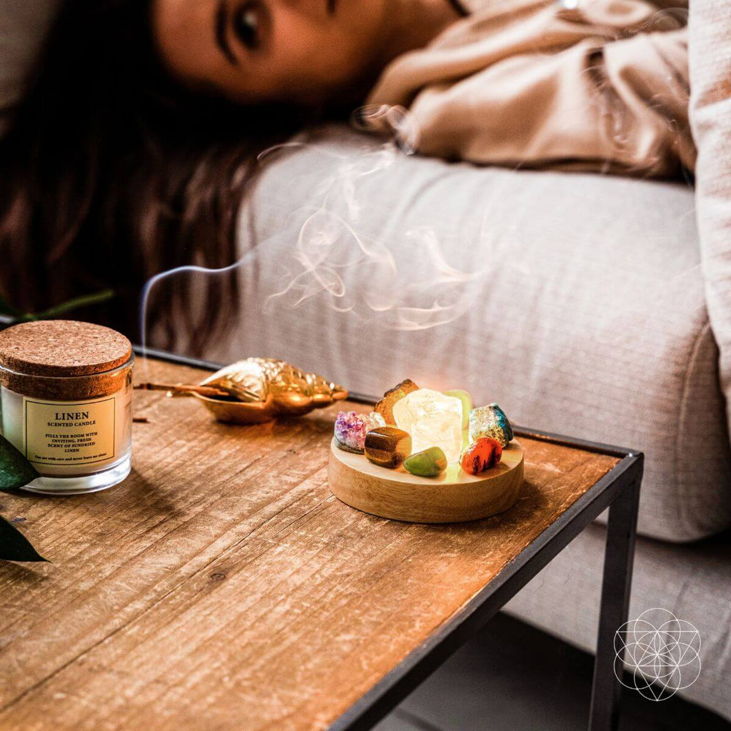 Glowing crystal display lamp on a wooden bedside table beside a candle, with a person resting in bed.
