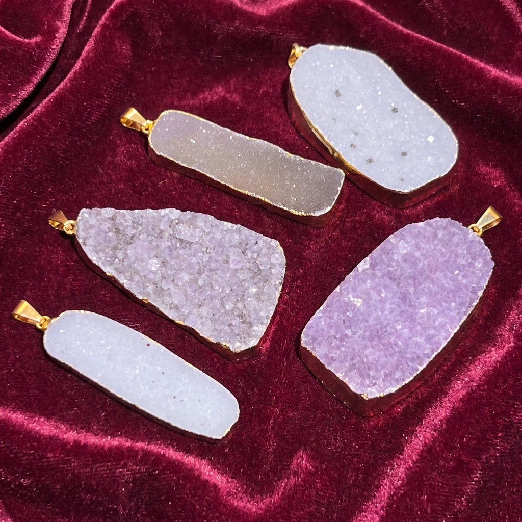 Five pale and lavender druzy crystal pendants with gold-plated edges and bails on burgundy velvet