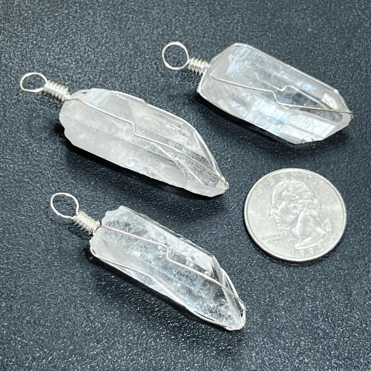 Three crystal pendants on a dark surface with a coin for scale.