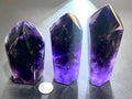 Three dark purple amethyst towers in ascending heights with backlit violet bases and a quarter for scale