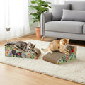 Two cats play with two cat scratchers in a bright living room. One cat is lying on a rectangular scratcher with a floral print, and the other is standing on a wedge-shaped scratcher.