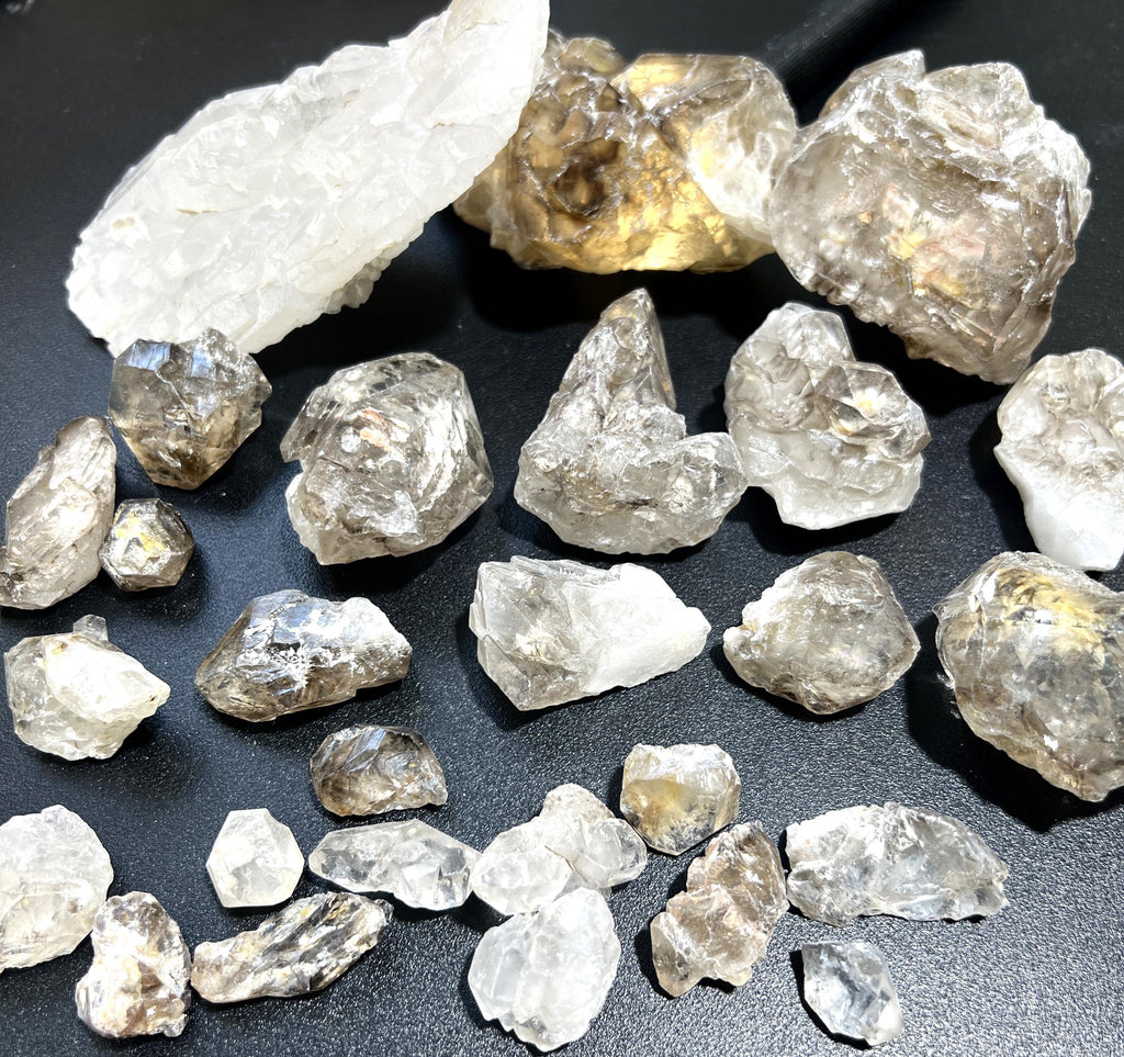 Assorted rough elestial alligator quartz clusters in clear, milky white and smoky tones on a dark surface