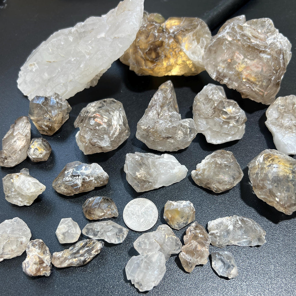 Mixed-size elestial alligator quartz clusters arranged on a dark surface with a coin for scale