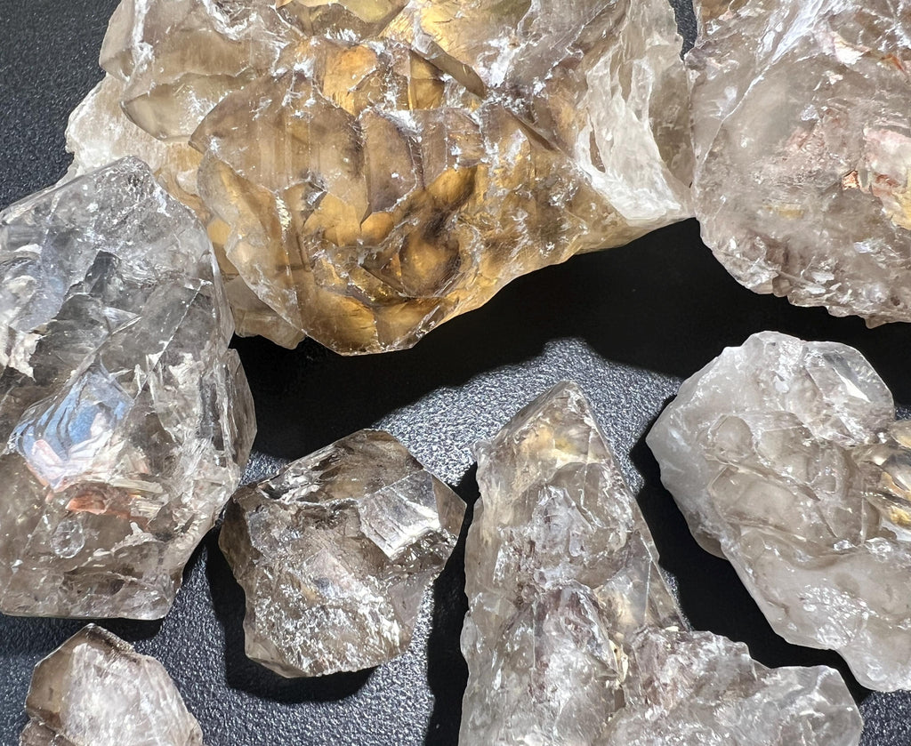 Detailed view of clear and smoky elestial quartz clusters with reflective ridges and a warm-toned specimen behind them