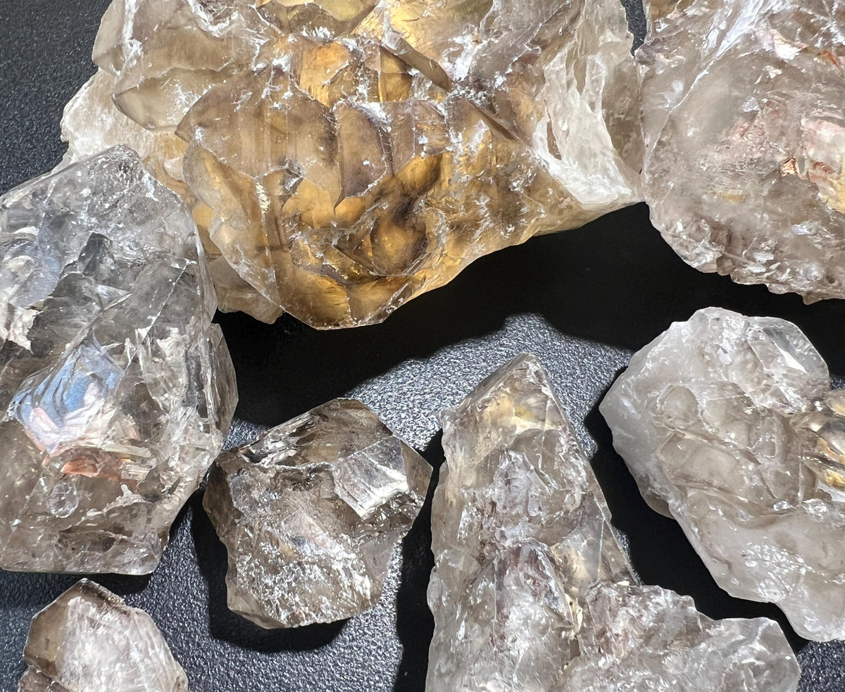 Detailed view of clear and smoky elestial quartz clusters with reflective ridges and a warm-toned specimen behind them