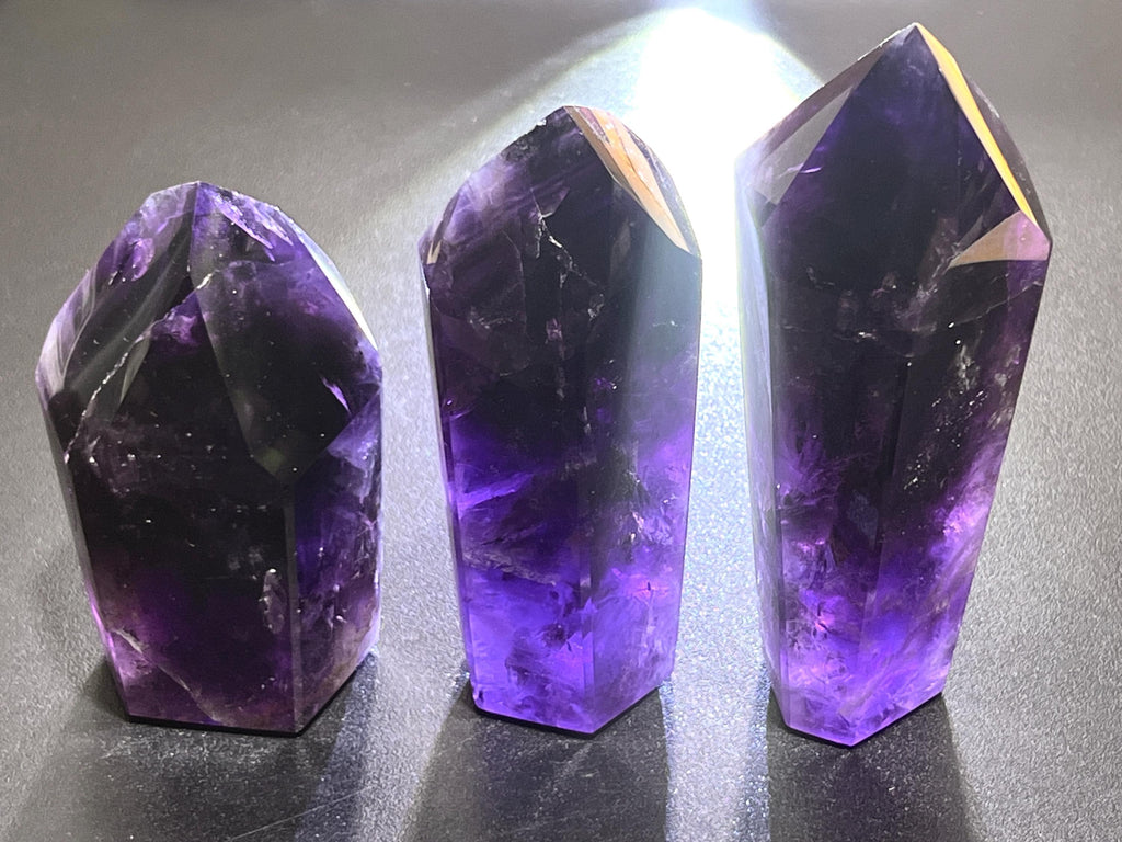 Three faceted amethyst towers with deep purple bodies and brightly backlit violet lower sections