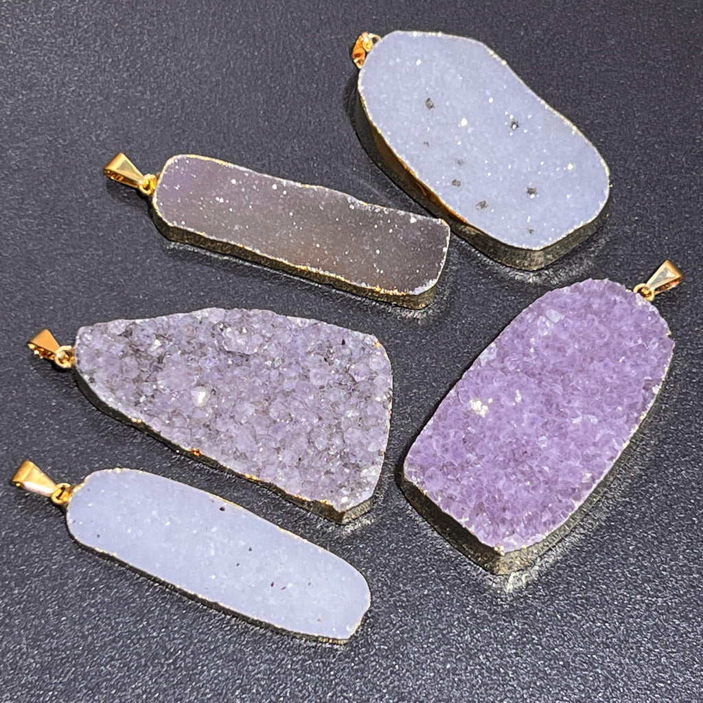 Five gold-edged druzy pendants with elongated and irregular shapes and sparkling pale and lavender surfaces
