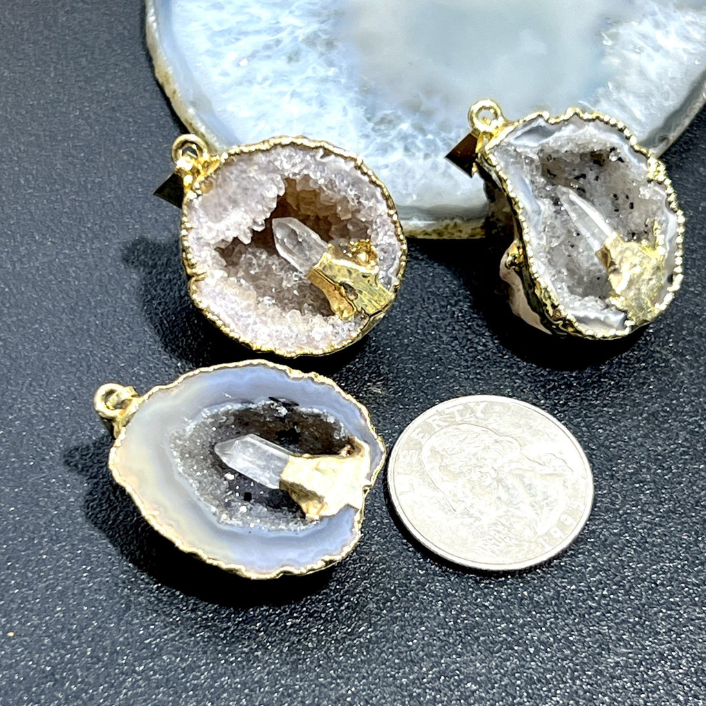  Three gold-plated Oco geode pendants with quartz points beside a quarter and a pale agate slice.