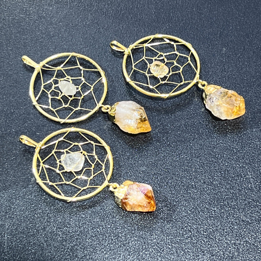 Three gold-plated dreamcatcher pendants with small center stones and dangling yellow citrine points on a dark background.
