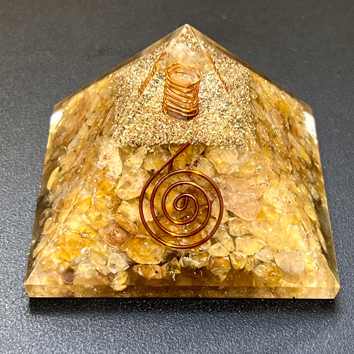 Front view of a golden yellow quartz resin pyramid showing crystal chips, a central spiral, and a coil near the tip.