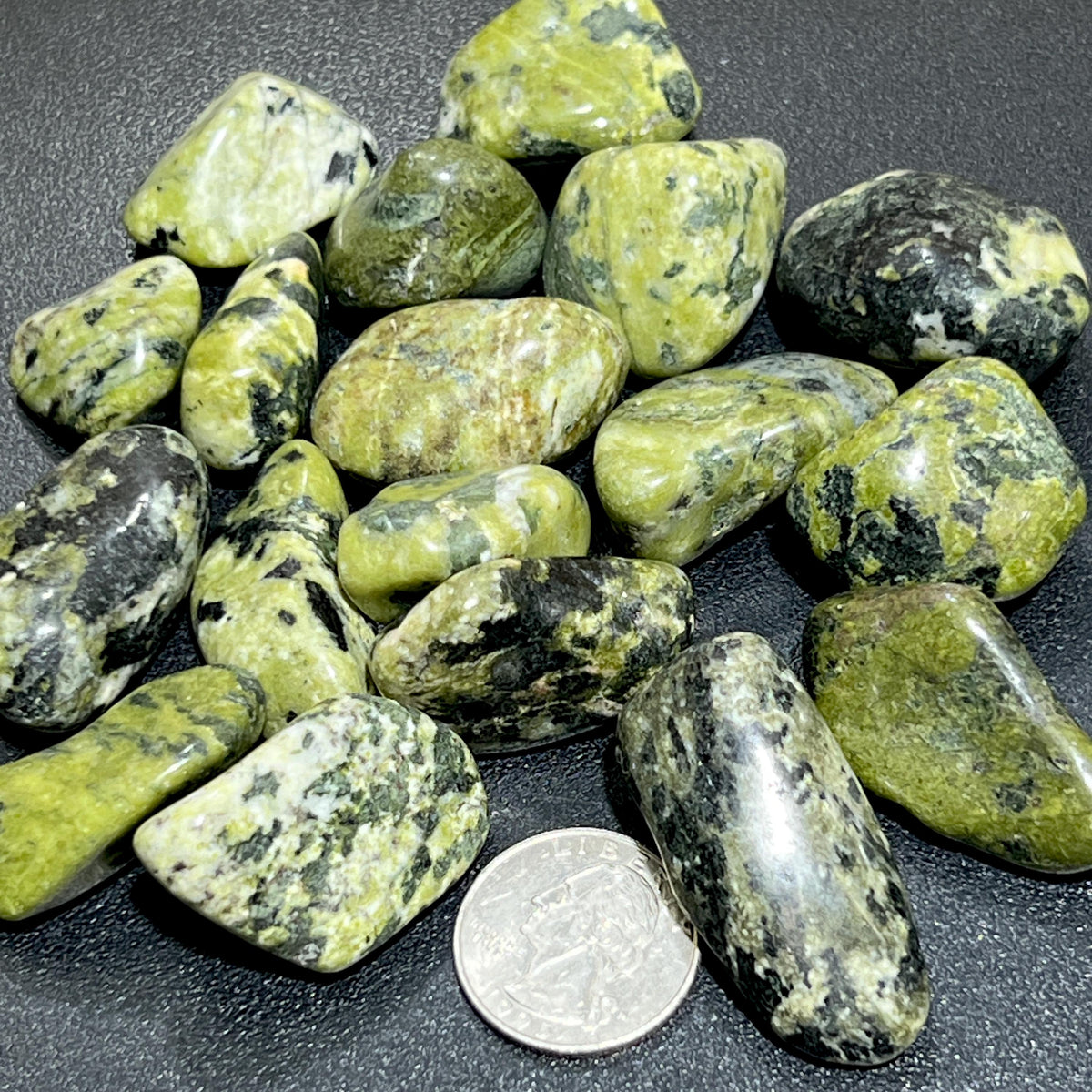 Assorted green nephrite jade tumbled stones with contrasting dark and cream markings beside a quarter for size comparison.
