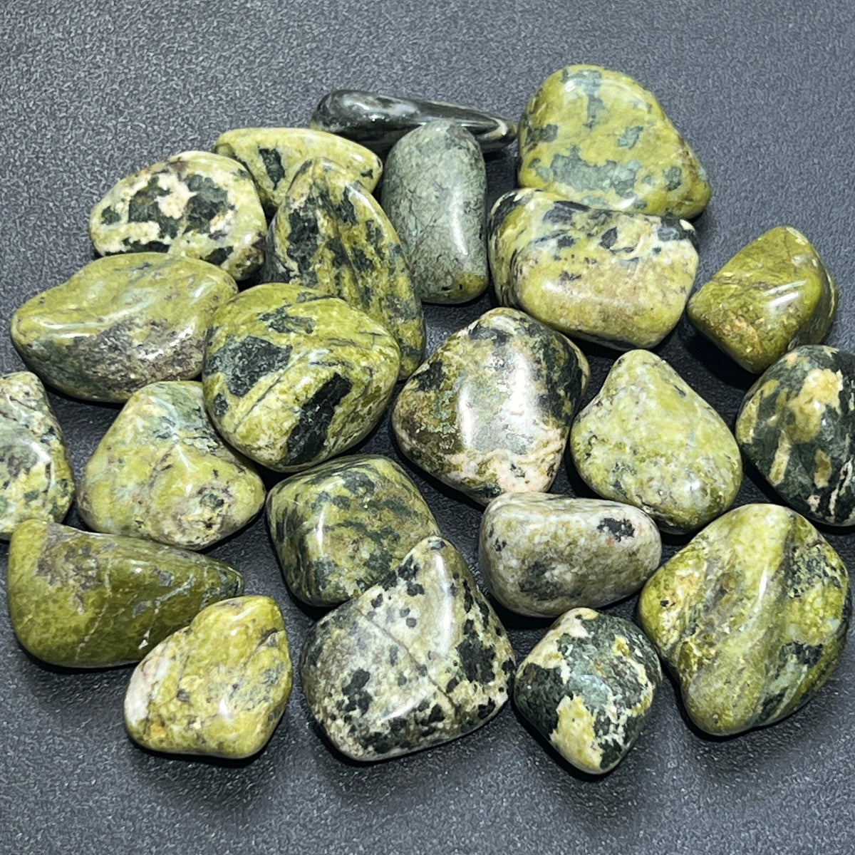 Polished green nephrite jade tumbled stones with olive, pale green, and dark mottled markings on a dark surface.