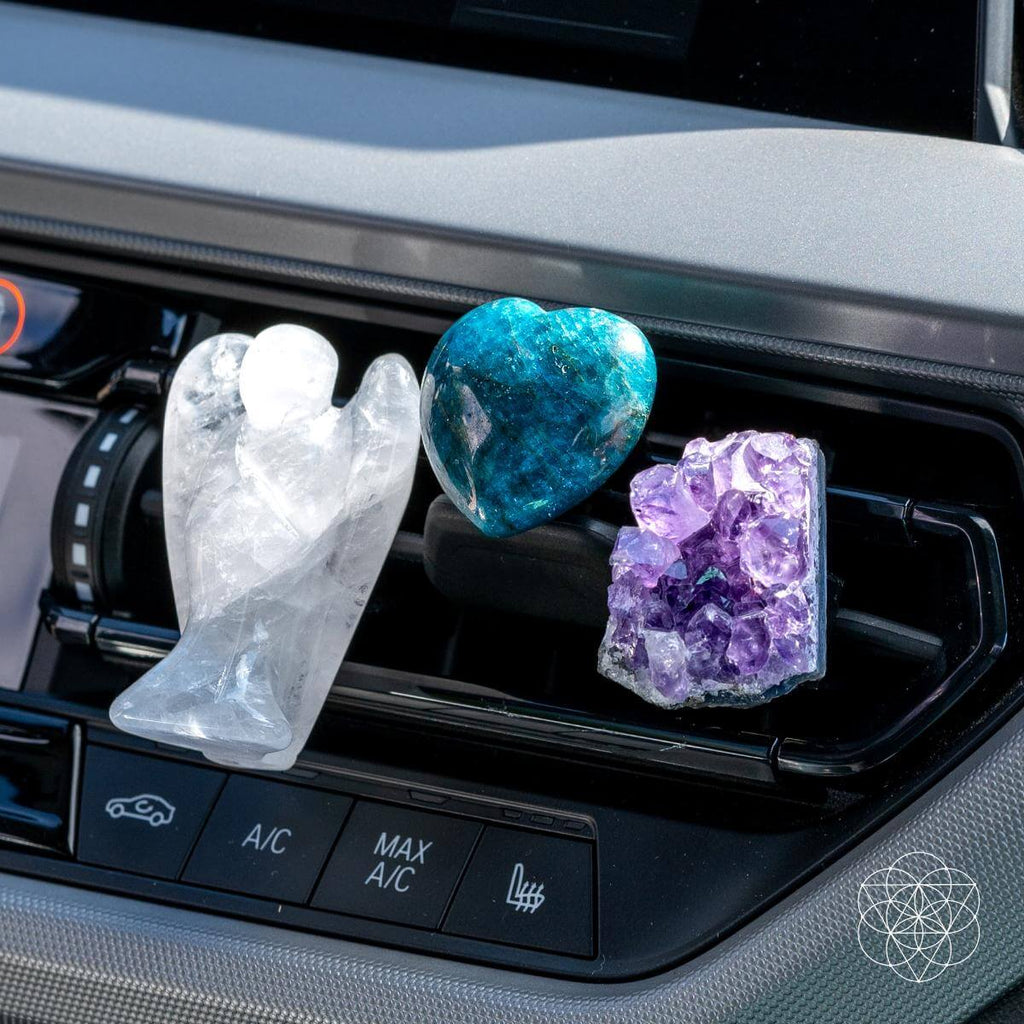 Angled close-up of three crystal car vent clips featuring a quartz angel, blue heart, and amethyst cluster.